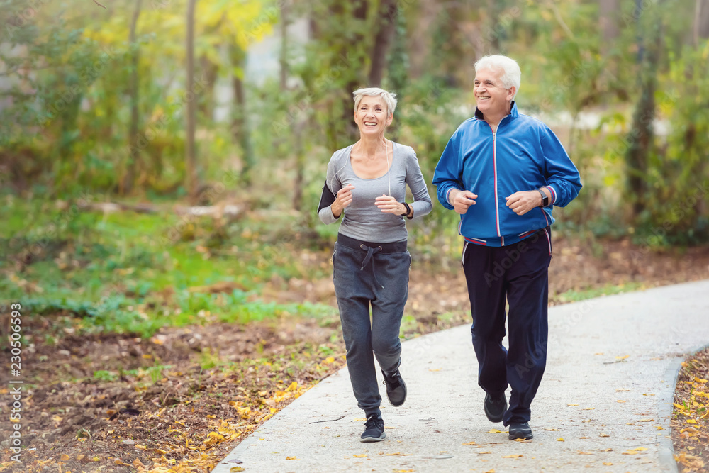 Smiling senior active couple jogging together in the park - obrazy, fototapety, plakaty 