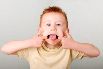 Fiery redhead young boy pulling a face, fingers in his mouth tongue sticking out