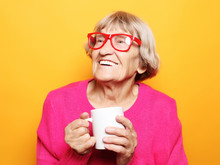Portrait Of Old Excited Lady Smiling Laughing, Holding Cup Drinking Coffee, Tea, Beverage On Yellow Background