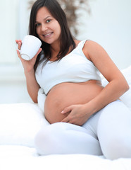 Wall Mural - happy pregnant woman drinking milk sitting in the living room.