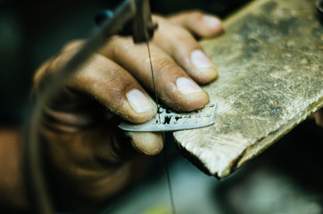 man's hands goldsmith work on a piece of silver with a metal saw on the work table, close up, selected focus, narrow depth of field