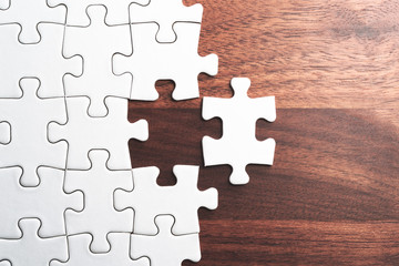 Aufkleber - Assembling jigsaw puzzle pieces. Abstract background.Unfinished white jigsaw puzzle pieces on wood table.