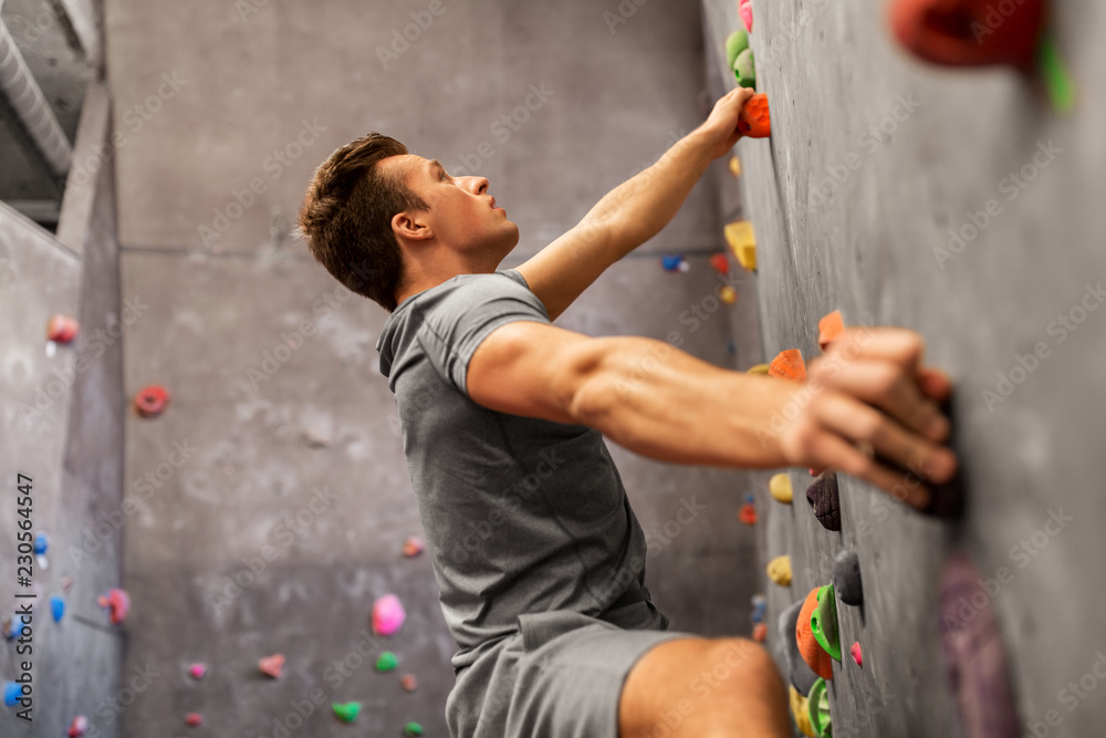 fitness, extreme sport, bouldering, people and healthy lifestyle concept - young man exercising at indoor climbing gym - obrazy, fototapety, plakaty 