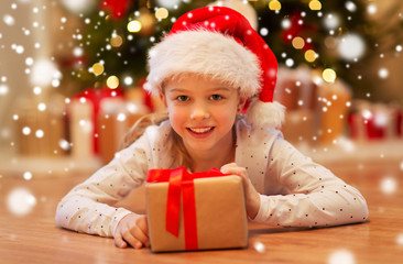 christmas, holidays and childhood concept - smiling girl in santa helper hat with gift box at home