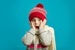 © Ilshat - Frightened little girl in red winter hat with pompom and wrapped a scarf, put her hands to cheek, expresses surprise and amazement, demonstrates the bright children emotion of stunning.