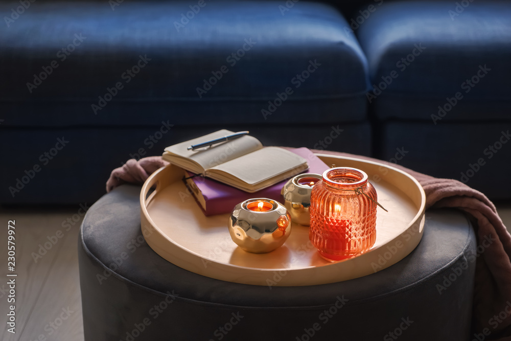 Composition with burning candles in decorative holders and notebooks on tray indoors