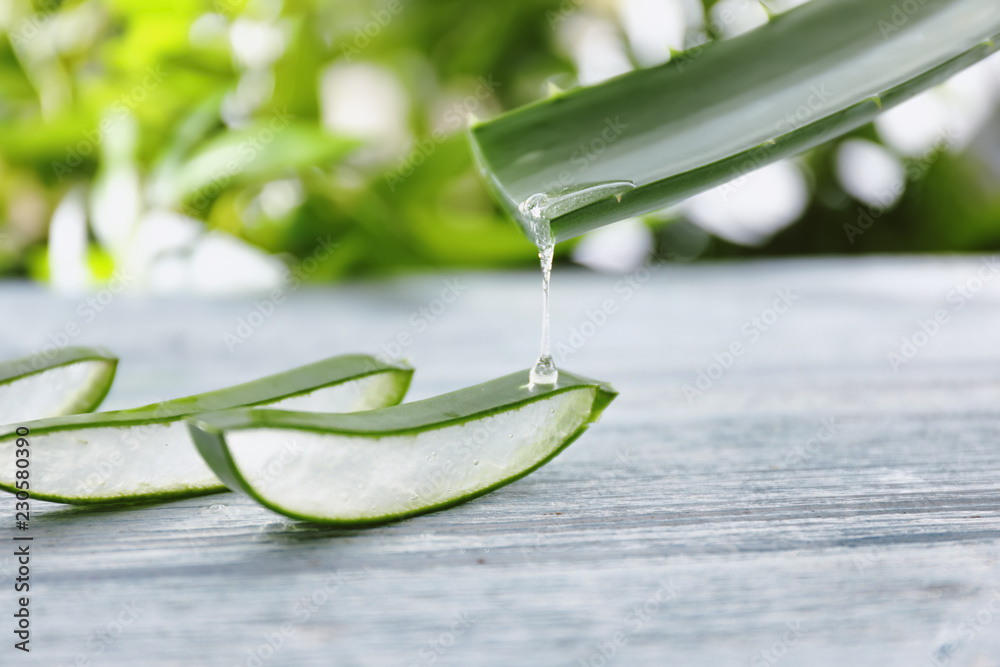 Aloe vera juice dripping from green leaf on wooden table