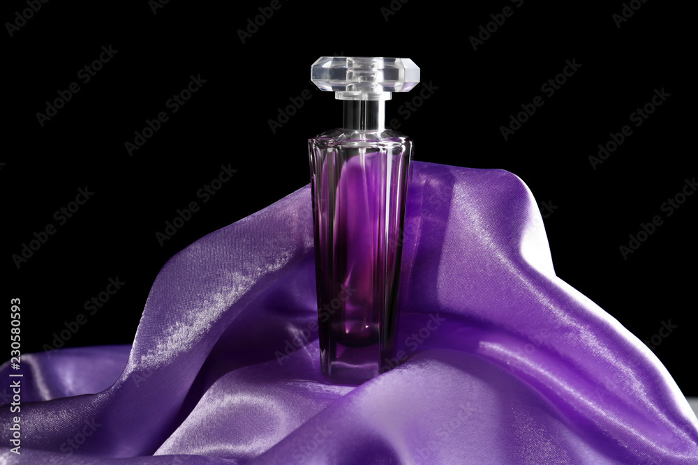 Bottle of perfume with shiny fabric on dark background