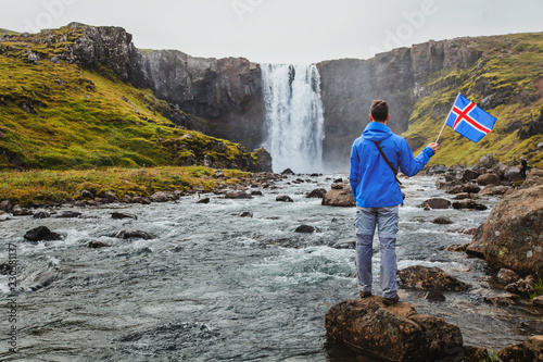 Fotografía travel to Iceland, tourist holding icelandic flag near scenic waterfall