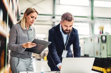 A portrait of an industrial man and woman engineer with laptop in a factory, working.
