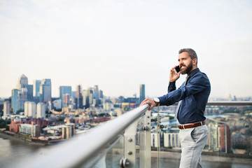 Poster - A portrait of businessman with smartphone standing against London view panorama.