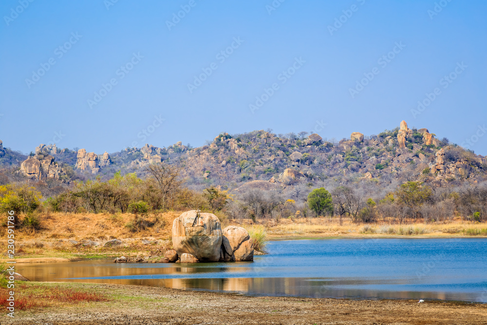 View of a lake surrounded by rocks, in Matobo National Park, Zimbabwe. September 26, 2016. - obrazy, fototapety, plakaty 