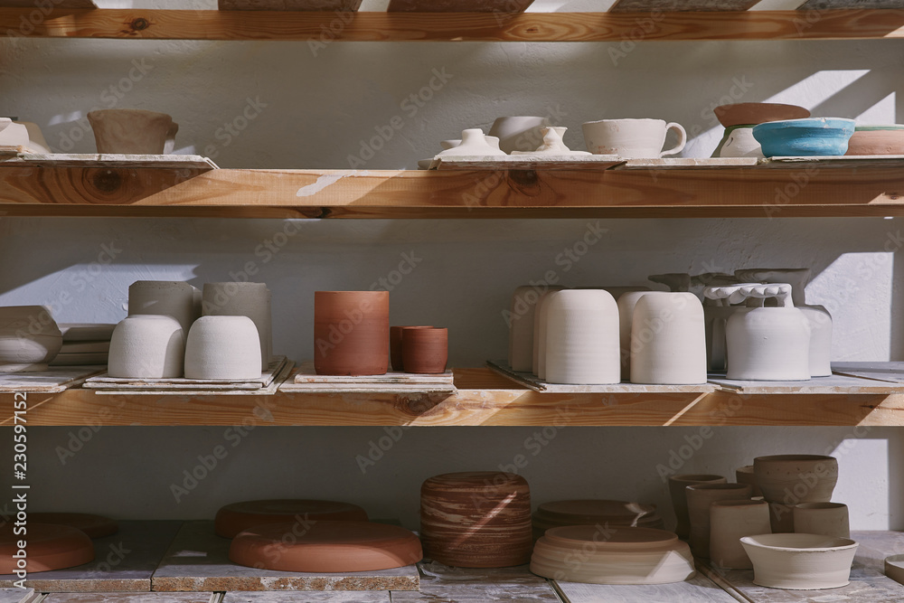 ceramic bowls and dishes on wooden shelves at pottery studio - obrazy, fototapety, plakaty 