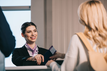 Wall Mural - cropped shot of airport worker giving passport with boarding pass to young woman at check-in desk