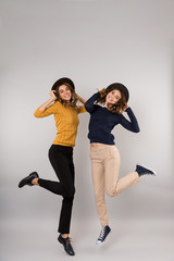 Wall Mural - Full length image of two brunette girls smiling and having fun together, isolated over gray background