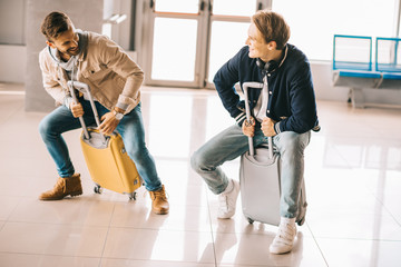 Wall Mural - happy young men riding suitcases and having fun in airport