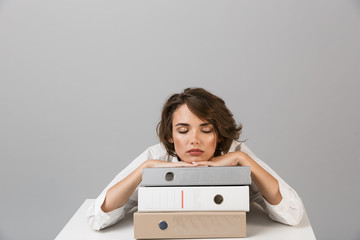 Sticker - Bored tired young woman sitting at the table isolated over grey background sleeping on folders.