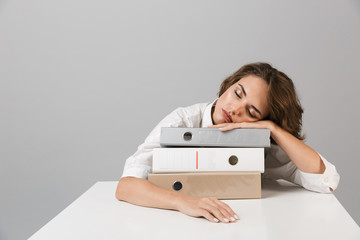 Canvas Print - Bored tired young woman sitting at the table isolated over grey background sleeping on folders.