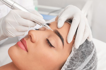 Young woman undergoing procedure of permanent eyebrow makeup in tattoo salon, closeup