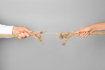 Wall Mural - Man and woman pulling frayed rope at breaking point on gray background