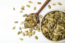Shelled raw pumpkin seeds in dish on white background, top view