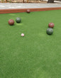 Five Bocce Balls and a pallino ball on a green bocce court.