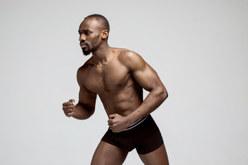 Fit young man with beautiful torso, isolated on gray background. The naked torso of African American man posing at studio. The muscular body, fitness, sports, healthy lifestyle and bodybuilder concept