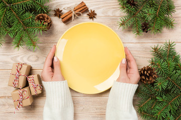 girl hand hold top view. empty yellow plate on wooden background with christmas decoration. new year