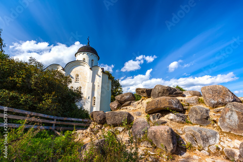 Fotografia, Obraz Ancient stones from the medieval tower Raskatnaya, ruins on the background of the Russian Orthodox Church in front of a wooden fence