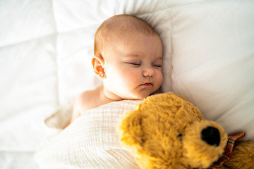 Wall Mural - A 4 month baby sleeping on a white bed at home with bear