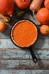 Wall Mural - Brightly colored pumpkin pie in cast iron pan surrounded with organic pumpkins and squashes on blue wooden background