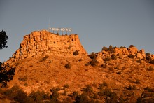 Low Angle View Of The City Of Trinidad Colorado Landmark Sign With An Early Sunrise Glow Against The Rocky Butte And Sky.