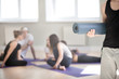 © fizkes - Group of millennial guys and girls wearing sportswear sitting together people talking communicating at sport seminar meeting, on foreground standing caucasian athletic man holding yoga mat close up