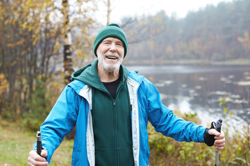 People, aging, healthy active lifestyle, well being, sports and leisure concept. Attractive cheerful bearded European mature male in his sixties spending day outdoors, having nordic pole walking