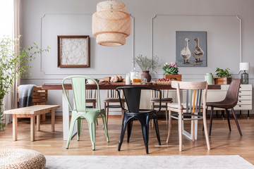 Different kid of chairs at table with flowers and food in rustic dining room interior with lamp and posters. Real photo