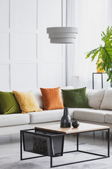 Vertical view of simple white chandelier hanging above modern wooden coffee table in living room with golden lime accents