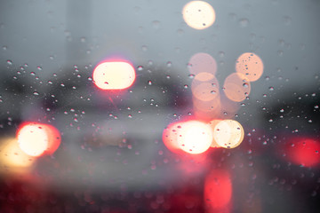 Drizzle rain drop on glass with street and cars lights at night blur bokeh abstract background. Raining season concept