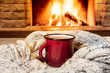 © larisa_stock - Cozy scene near fireplace with a Red enameled mug with hot tea and cozy warm scarf.