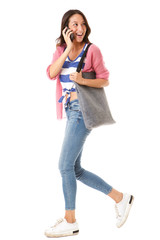 side portrait of happy young asian woman walking with purse and talking on cellphone against isolated white background