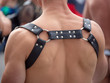 © David Tran - Black leather BDSM bondage harness on tone back of white man at outdoor crowded area