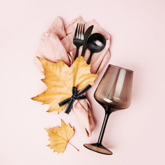 Wall Mural - Festive table setting with cutlery, pale pink napkin, black  wine glass and autumn leaves on pastel background. Flat lay, top view