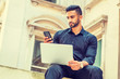 © Alexander Image - Way to Success. Young East Indian American Man with beard working in New York, wearing black shirt, holding laptop computer, sitting outside old style office building on campus, texting on cell phone.