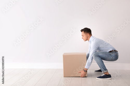 Cuadros en Lienzo Full length portrait of young man lifting heavy cardboard box near white wall