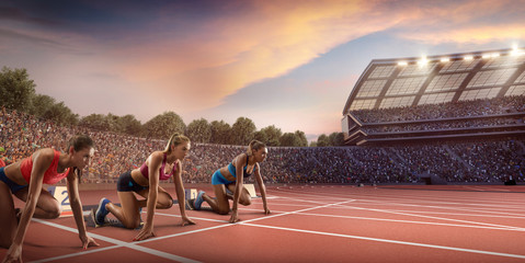 Wall Mural - Female athletes sprinting. Three women in sport clothes on starting line prepares to run at the running track in professional stadium