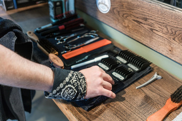 Close-up of the hand of a barber, choosing an useful tool from an open hair cutting kit placed on a wooden shelf in the interior of a hair salon for men