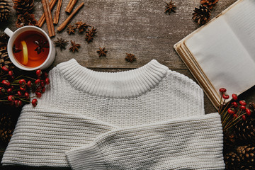 Wall Mural - flat lay with white sweater, red holly berries, cinnamon sticks, blank notebook and cup of tea on wooden surface