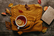 flat lay with fallen leaves, cup of tea with lemon pieces, book and orange sweater on wooden tabletop