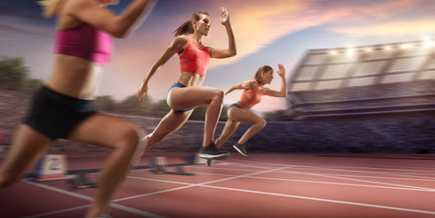 Wall Mural - Female athletes sprinting. Three women in sport clothes run at the running track in professional stadium