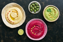 A Variety Of Colored Hummus, Classic Hummus, Beet Hummus, Hummus With Avocado On A Dark Rustic Background. Top View, Flat Lay. Clean Eating, Dieting, Vegetarian Party Food