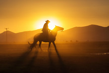 Silhouette Of A Cowboy With His Dog At Sunset And Dusts In Background